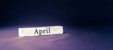 April, name of the month written on vintage white wooden block on purple blue textured background . Banner format.の写真素材