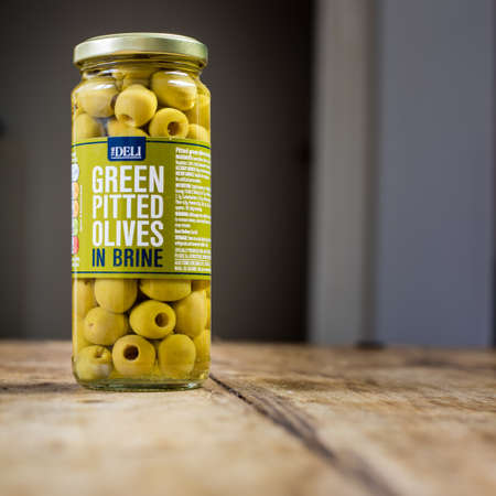 Perth, Scotland - 11 November 2019: Green pitted olives in brine isolated on vintage wooden tableのeditorial素材