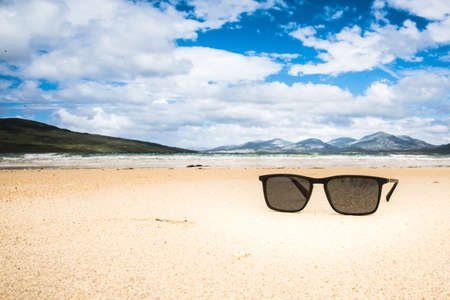 Sunglasses on sandy beach in summer - mountains, ocean and blue skyの写真素材