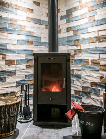 Modern wood burning stove. Tiled wall behind, stove with fire burning inside, cosy and warm interior scene, heating in winter.の写真素材