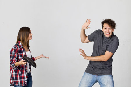 Young couple arguing in kitchen. Frustrated wife with cooking pan screaming to her husband