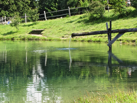 Mountain lake with water running over wooden channelの写真素材