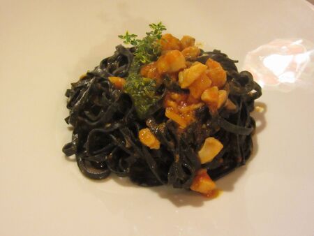 Cooked italian black noodles with squid sepia ink, pieces of squid, tomato sauce and pistachio sauce on plateの写真素材