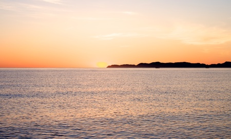 Sunrise over water with the sun at the tip of Carmen Island in Mexico.の写真素材