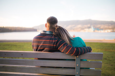 Young couple sitting on a bench in the park and looking at the lakeの写真素材