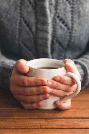 Woman sat at table with mug of tea wearing cozy gray cardiganの写真素材