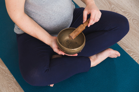 Pregnant woman doing prenatal yoga meditating with Tibetan singing bowlの写真素材
