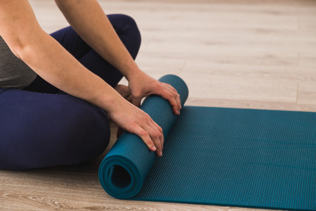 Woman sat cross legged in yoga studio rolling her matの写真素材