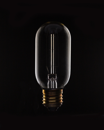 Unlit tungsten filament light bulb on a black background.の写真素材