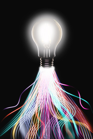 Innovation and ideas concept showing a lit light bulb with glowing trails of multi colored light leading to it, indicating all the individual factors that make up a great idea.の写真素材