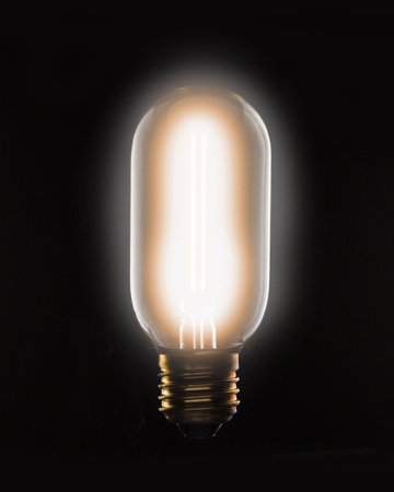 Long light bulb with lit tungsten filament on a black background.の写真素材