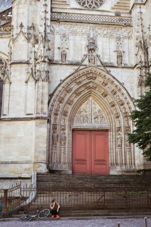 Bordeaux, France - Man on his phone sits on steps of Basilique Saint Michel with his bike next to him.のeditorial素材