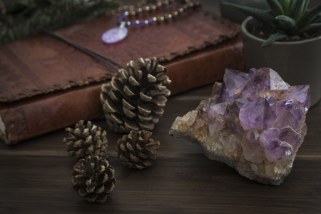 Large piece of amethyst crystal with leatherbound notebook plants and pine cones placed on wooden surfaceの写真素材