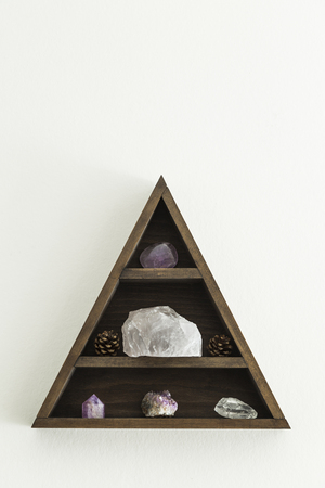 Wooden triangular crystal shelf with stones and pine cones hung on wallの写真素材