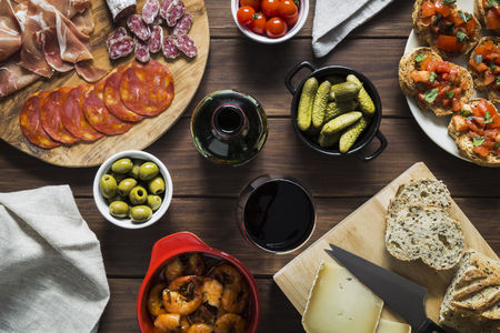 Table set with various tapas dishes and wine, including charcuterie and meat, olives, garlic prawns, cherry tomatoes, gherkins, bread and cheese and toasts.の写真素材