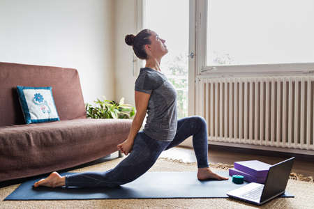 Yoga instructor or student in downward facing dog posture participating in online video lesson over...
