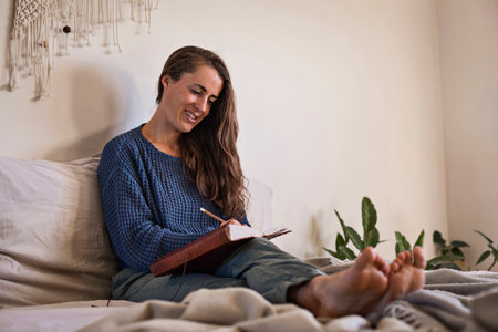 Woman sat writing in her leatherbound diary in bedの写真素材