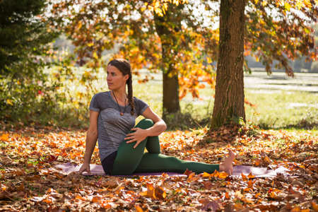 Woman practicing yoga among fall leaves and autumnal colours, in a park next to a lake
