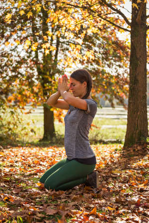 Woman practicing yoga in autumn in prayer posture, surrounded by yellow and golden fall leaves and...