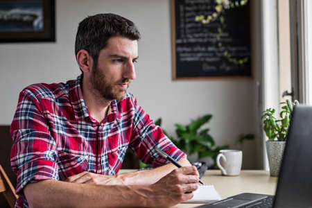 Businessman concentrating and doing work at home, using laptop and pen and notepadの写真素材