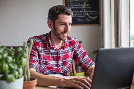 Smiling man typing on laptop at homeの写真素材