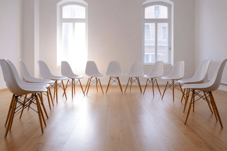 Bright white room with wooden floor and chairs arranged in a circle, representing discussion, therapy, meetings, or support group.の素材