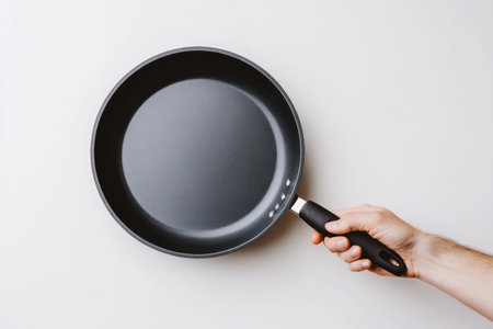 A strong hand grips a frying pan against white backdrop, showcasing utensil design and kitchen tool functionality.の素材