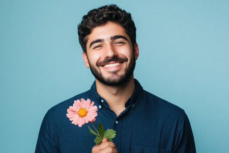 Portrait of a cheerful adult man holding a flower, symbolizing affection, kindness, and happiness, on a clean solid backdrop.の素材