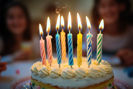 A birthday cake is topped with colorful twisted candles burning brightly, set in a joyful party with warm ambient lighting.の素材