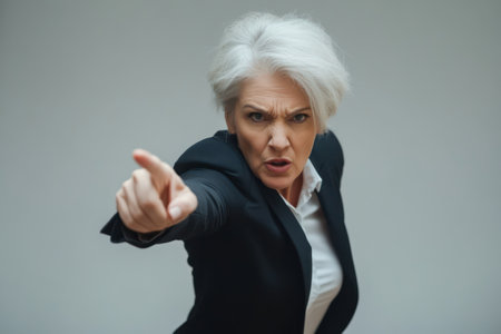 Older businesswoman in formal suit runs and points with a furious face, expressing urgency, anger, and corporate tension.の素材