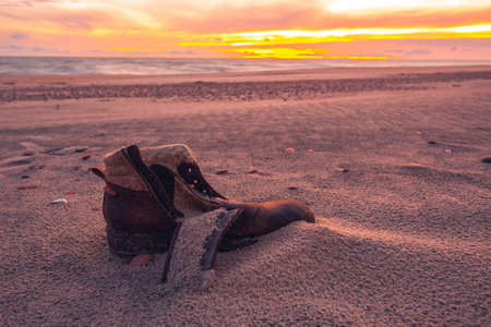 Old used boot lie half buried in desert sand dune in the evening lightの写真素材
