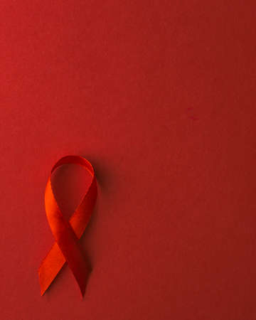 Red bow ribbon symbol HIV, AIDS cancer awareness with shadows, studio shot isolated on red background, Healthcare medicine concept, World AIDS Dayの写真素材