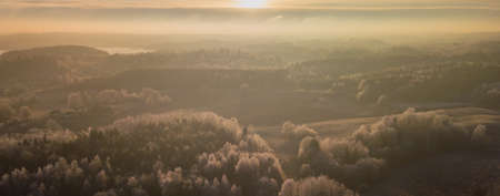 Aerial view from above of a countryside landscape with beautiful sunset light on a winter evening with forzen meadows and mist hazy horizon, bannerの写真素材