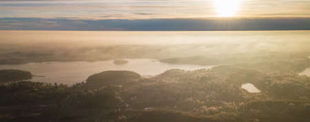 Aerial view from above of a countryside landscape with beautiful sunset light on a winter evening with forzen meadows and mist hazy horizon, bannerの写真素材