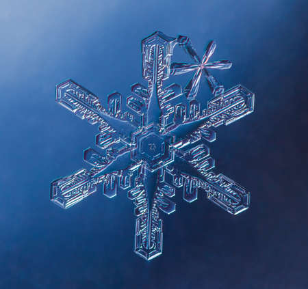 Snowflake on smooth gradient background. Macro photo of real snow crystal on glass surface. This is small snowflake with unusual pattern.の写真素材