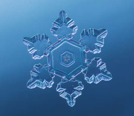 Snowflake on smooth gradient background. Macro photo of real snow crystal on glass surface. This is small snowflake with unusual pattern.の写真素材