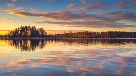 Epic red sunset sky above the lake and forest. Dramatic cloudscape. Symmetry reflections on the water, natural mirrorの写真素材
