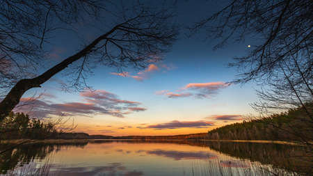 Epic red sunset sky above the lake and forest. Dramatic cloudscape. Symmetry reflections on the water, natural mirrorの写真素材
