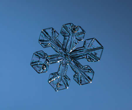 Snowflake on smooth gradient background. Macro photo of real snow crystal on glass surface. This is small snowflake with unusual pattern.の写真素材