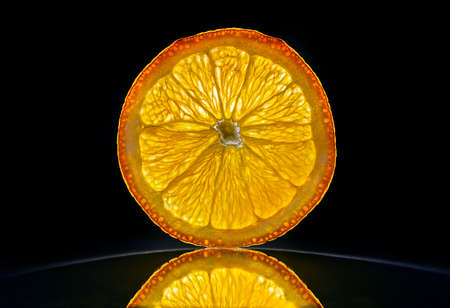 Slice of a orange isolated in dark black bacnground with reflectionの写真素材