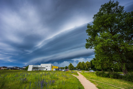 Dramatic storm clouds over rural house and green field create ominous atmosphere