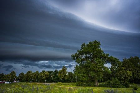 Dramatic storm clouds over rural house and green field create ominous atmosphere