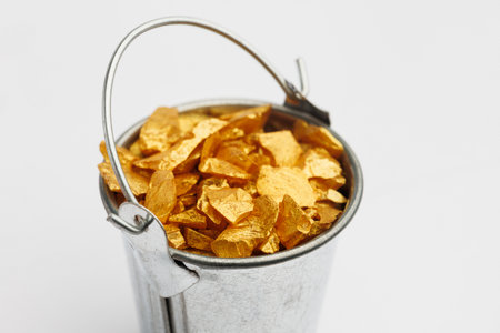 Small metal bucket filled with golden stones on white background. Concept of wealthの写真素材