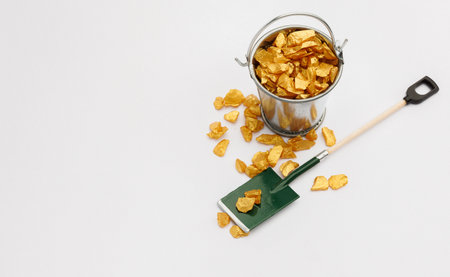 Small metal bucket filled with golden stones on white background.