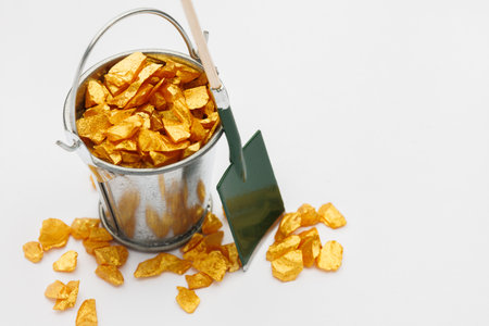 Small metal bucket filled with golden stones on white background. Concept of wealthの写真素材