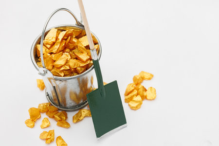 Small metal bucket filled with golden stones on white background. Concept of wealthの写真素材