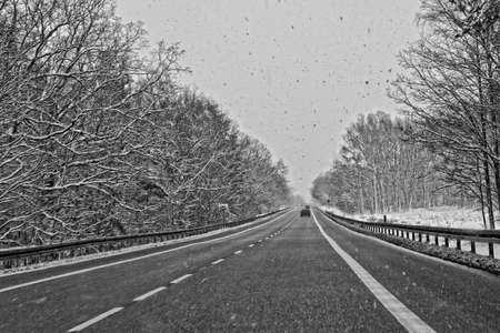 wide winter road outside the city during snowfallの写真素材