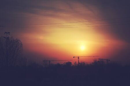 beautiful colorful sunset with red sky, trees and clouds and construction crane