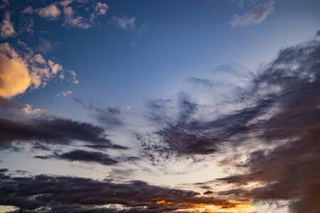 beautiful evening blue sky with dark clouds lit by the orange sun