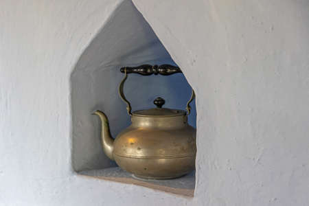 old brass antique kettle on a white brick shelf